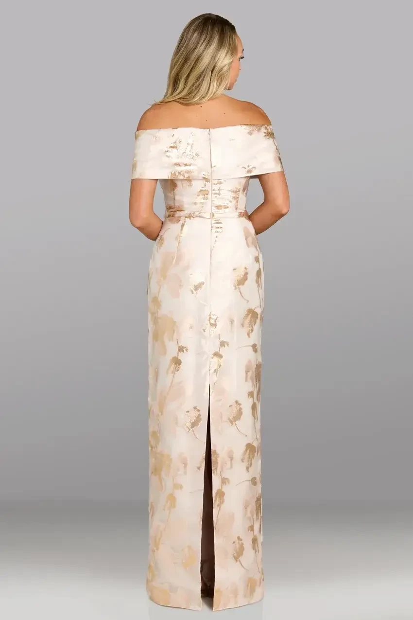 A woman in an elegant off-the-shoulder dress with a floral pattern, photographed from the back. The dress has a fitted bodice and a long slit at the back.