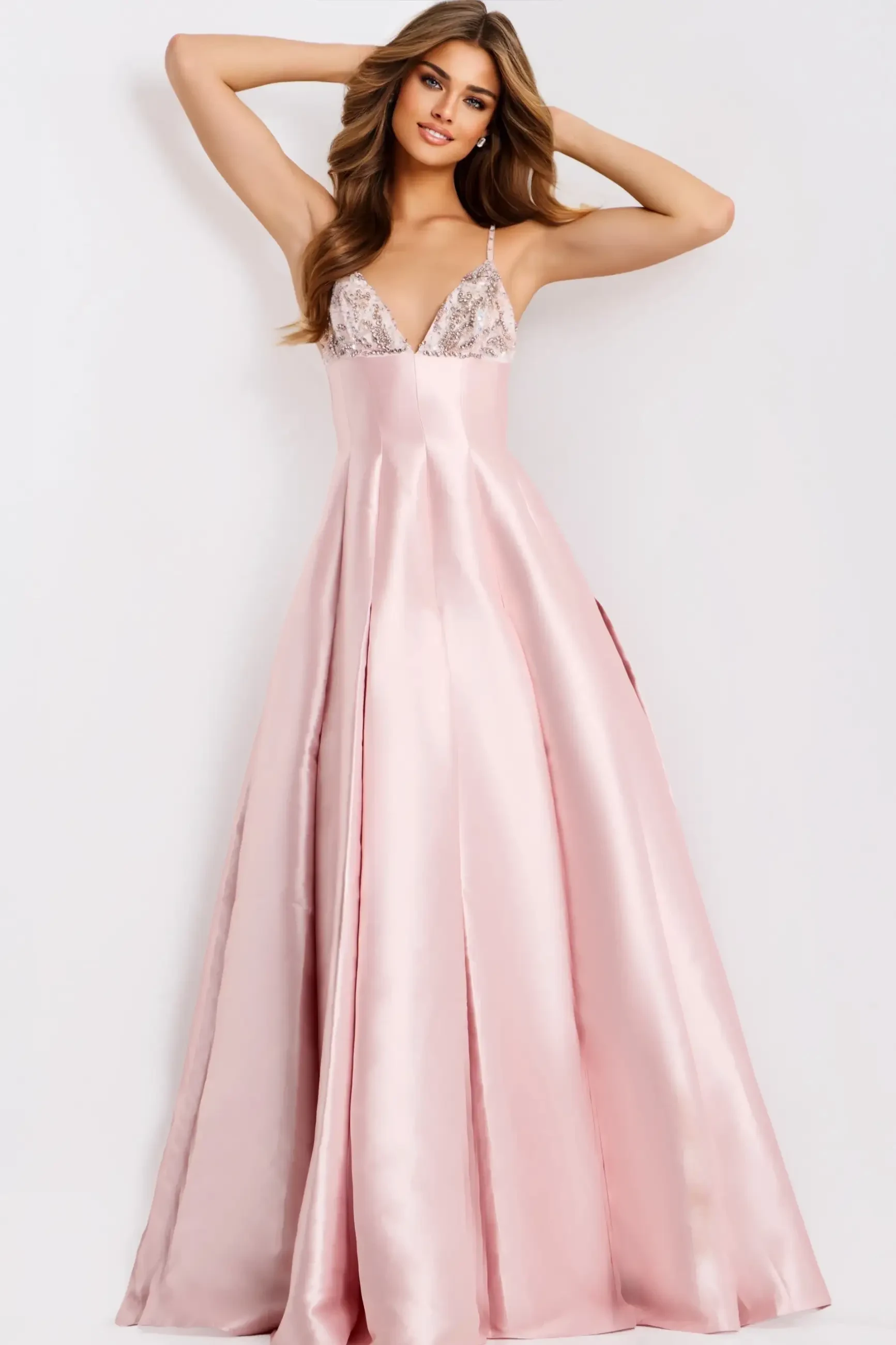 A woman wearing a long, elegant pink dress with a fitted bodice and flowy skirt, striking a pose with her arms raised.